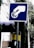 A blue and white sign depicts a hand inserting a coin into a slot or meter. The background includes a building, trees, and a utility pole with wires.