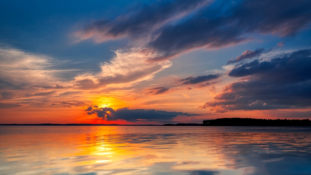 the sun is setting over a calm lake