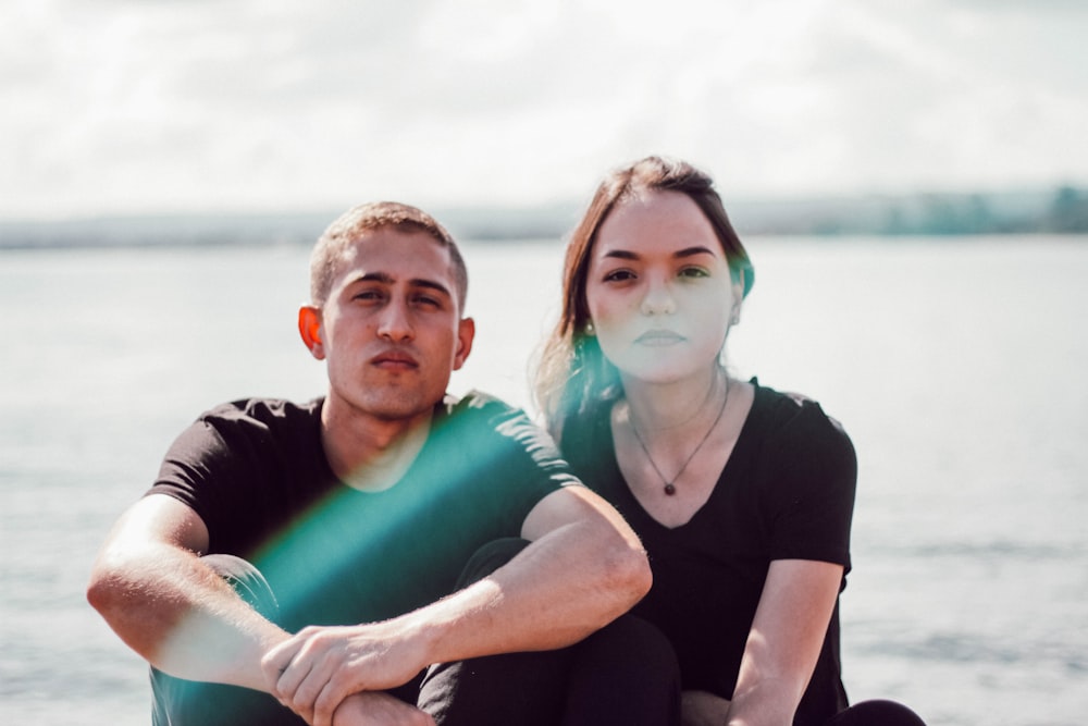 man and woman couple in black shirts sitting in beach