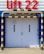 A large set of white industrial doors with handles, framed by sturdy blue metal. Above the doors, a bright red sign reads 'Lift 22' in bold letters. A yellow and black striped barrier runs horizontally above the doors, with matching striped poles on either side, adding a sense of caution. The ground is paved with concrete bricks.
