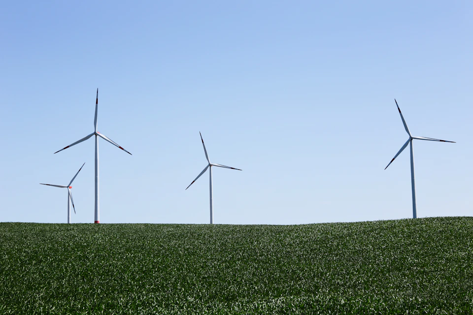 Four wind turbines stand on a grassy hill amidst a serene landscape under clear skies