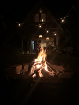 A cozy cabin lit warmly at dusk, nestled among tall trees with a hammock outside.