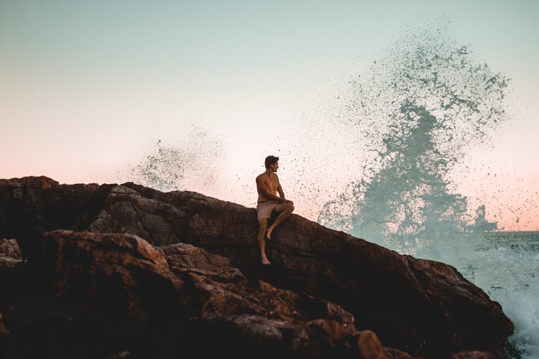 topless man sitting on the rock cliff near the ocean