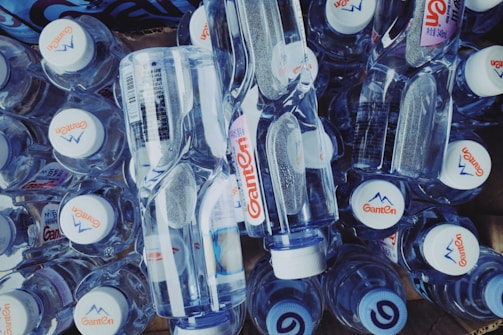 A collection of clear plastic water bottles with white caps, featuring a logo and design on the label, arranged in a compact layout.