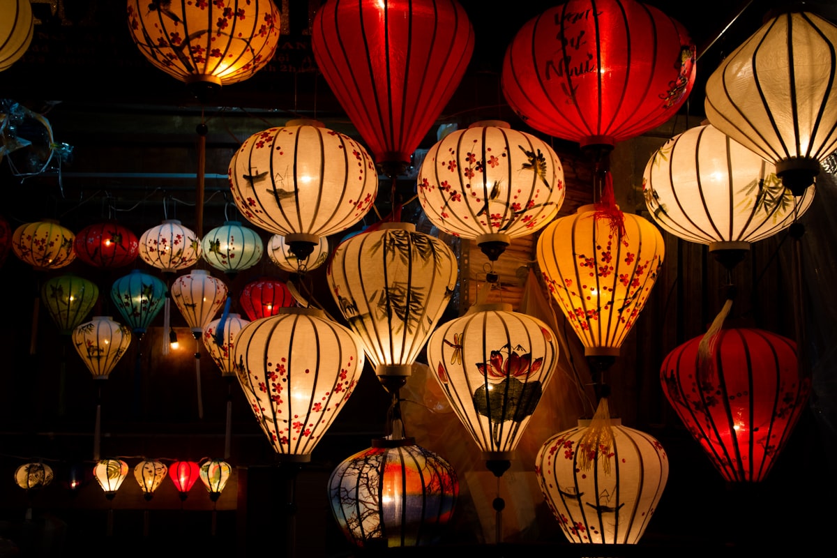 Hoi An July — assorted-colour silk lanterns glowing at night above the crowded Ancient Town streets at peak summer