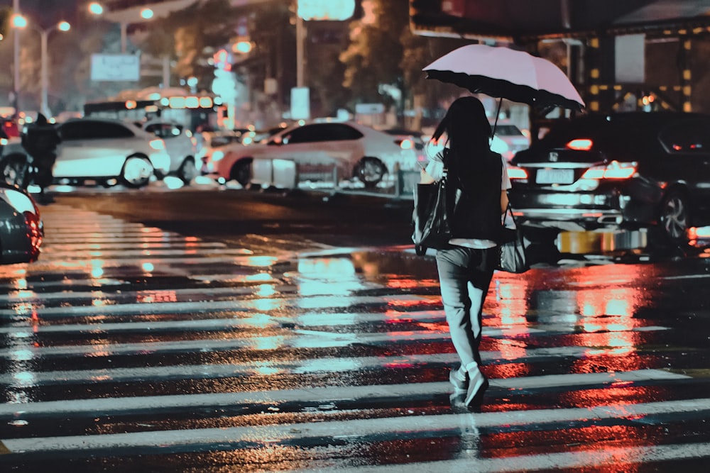 woman using umbrella crossing on pedestrian lane during nighttime