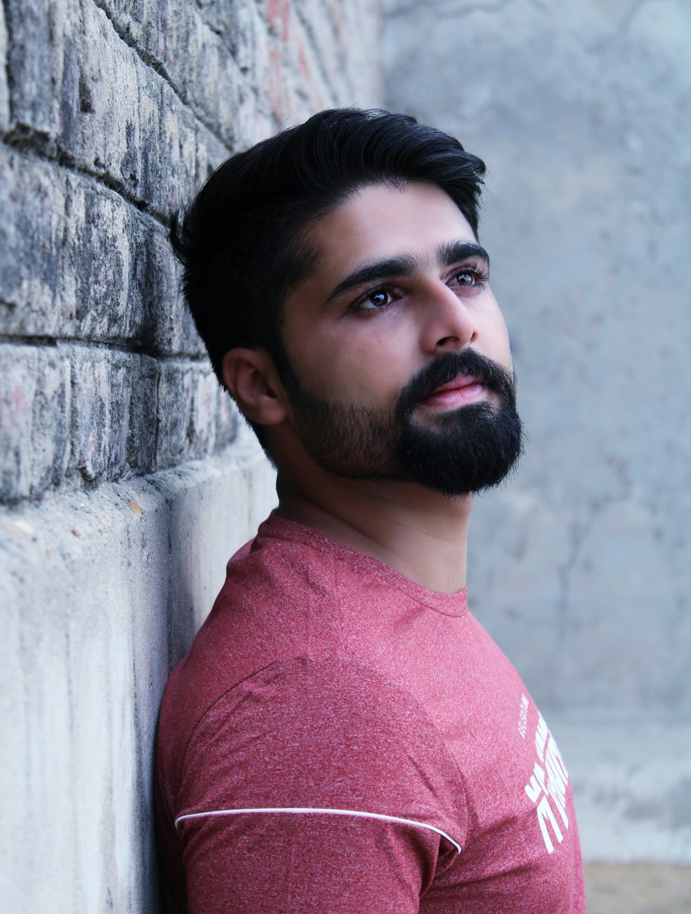 man in red shirt standing and leaning on concrete wall