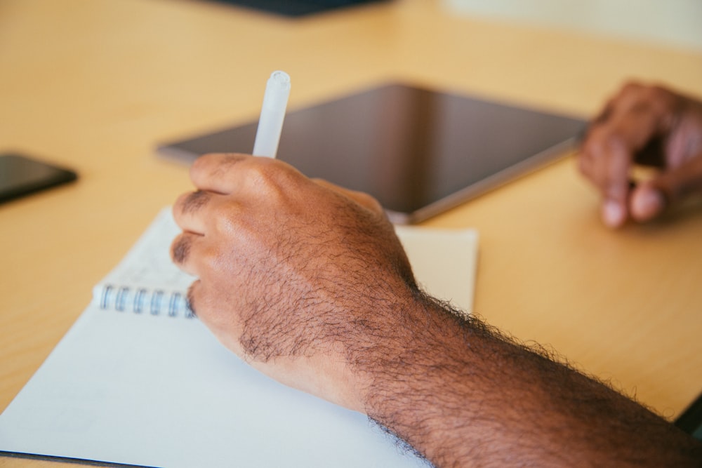 person holding pen writing on book