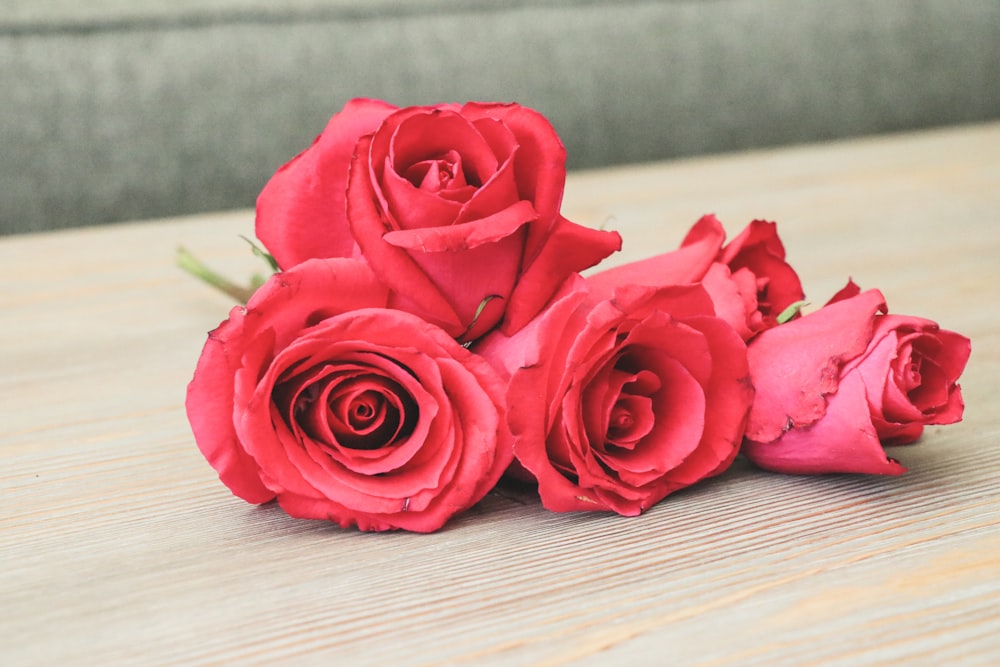 Un ramo de rosas rojas sentado encima de una mesa de madera