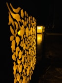 A pattern of floral cutouts illuminated from behind by warm yellow light. The intricate design casts shadows and creates a contrast against the dark, surrounding environment. The flooring appears to be marble, adding to the elegant and ambient setting.