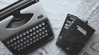 A vintage typewriter next to a stack of old books on a wooden table.