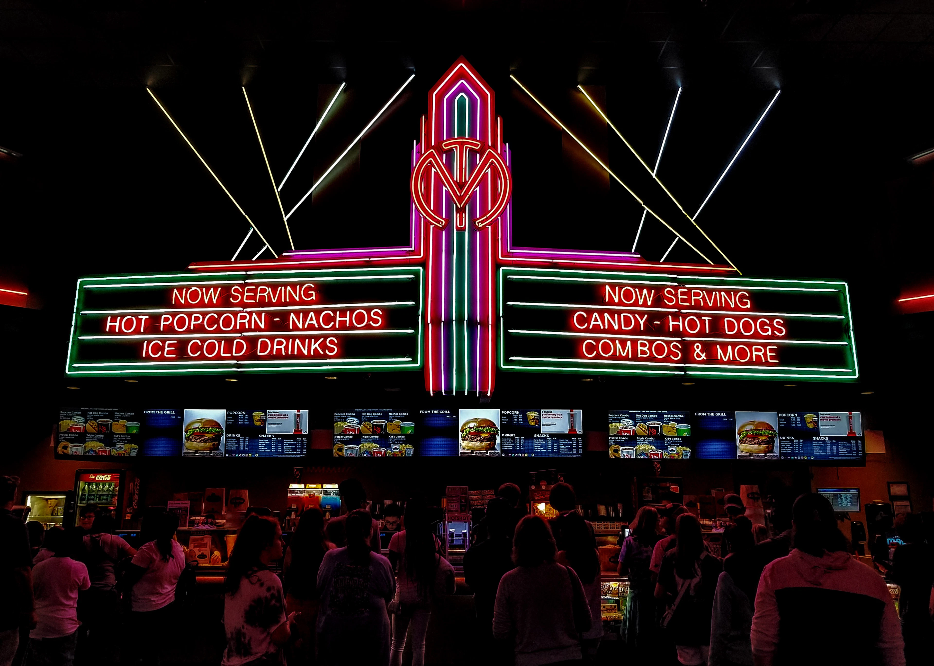Façade de cinéma illuminée de néons, la nuit, avec une foule devant l'entrée