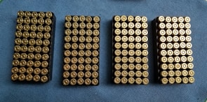Four rectangular trays filled with neatly arranged brass-colored bullets are placed on a blue textured surface.