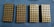 Four rectangular trays filled with neatly arranged brass-colored bullets are placed on a blue textured surface.