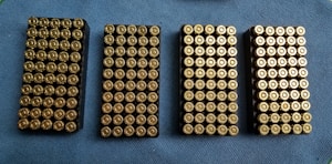 Four rectangular trays filled with neatly arranged brass-colored bullets are placed on a blue textured surface.