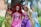 Four dolls dressed as princesses are standing in an outdoor setting with greenery in the background. Each doll has distinct hair color and is wearing a decorative gown in various shades of yellow, pink, purple, and blue.