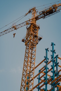 A crane lifting steel beams against a clear blue sky during a sunny day.