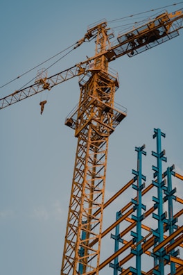 A construction crane lifting steel beams against a clear blue sky.