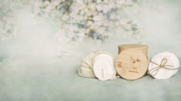 A soft pastel background with blurred floral patterns is the backdrop for a set of eco-friendly cosmetic pads and bamboo containers. The pads appear soft and are wrapped with a twine. The bamboo container displays a cute panda logo, emphasizing an eco-friendly theme.
