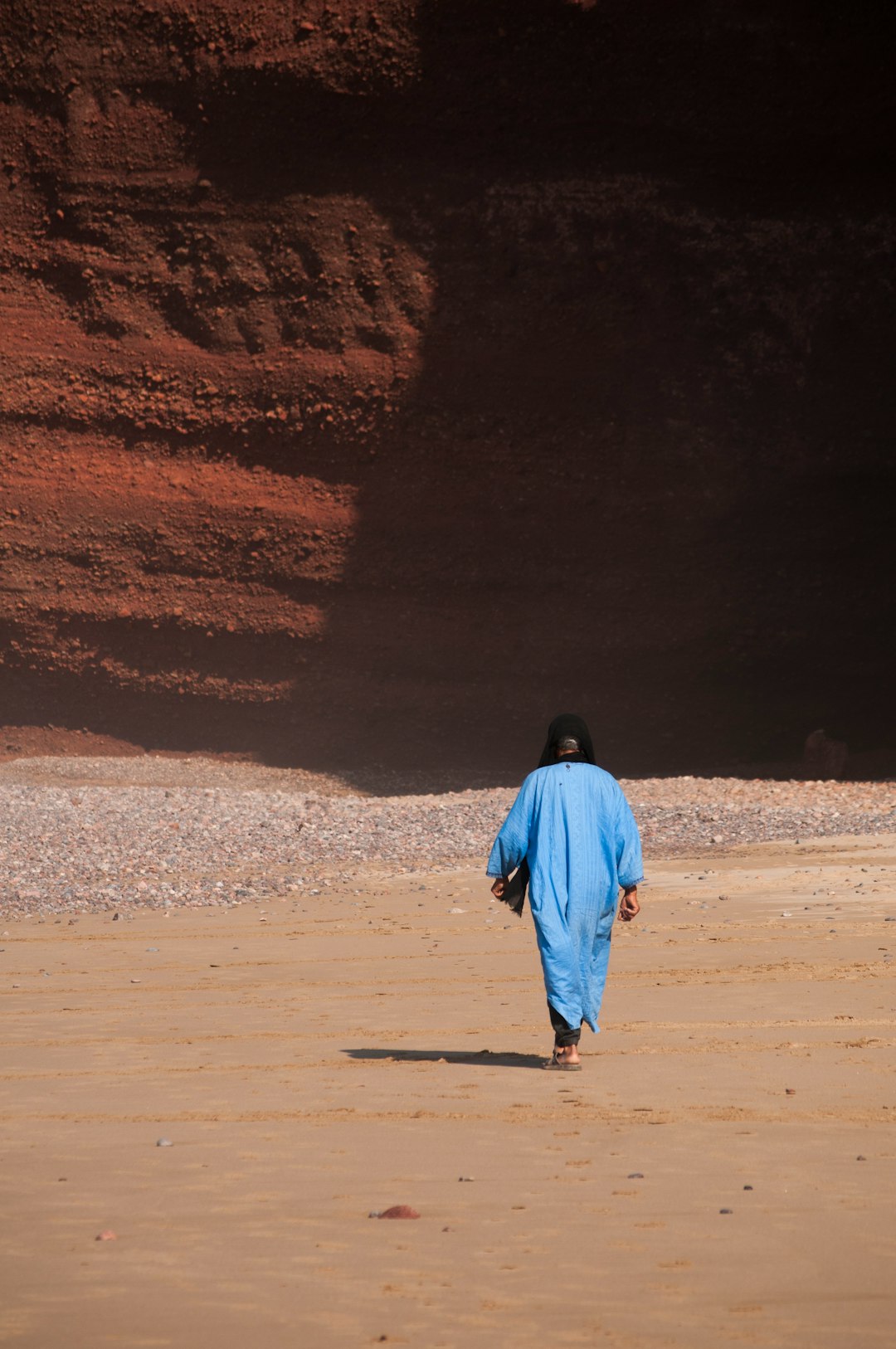 person in blue tunic walking on sand