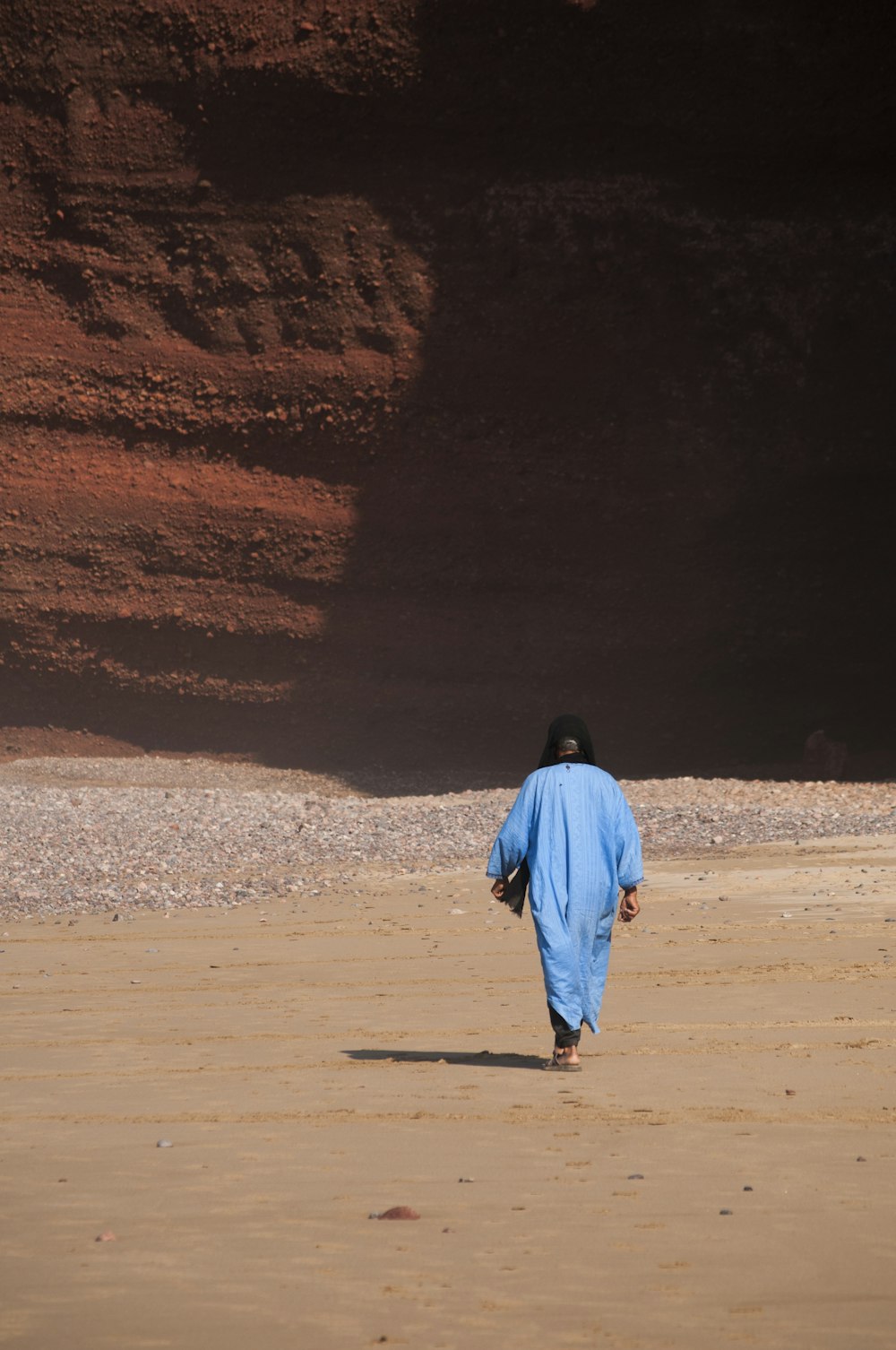 person in blue tunic walking on sand
