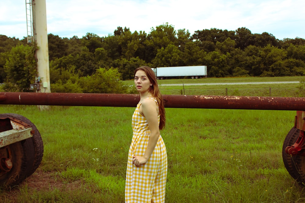 woman looking over her left shoulder standing on grass beside pipe