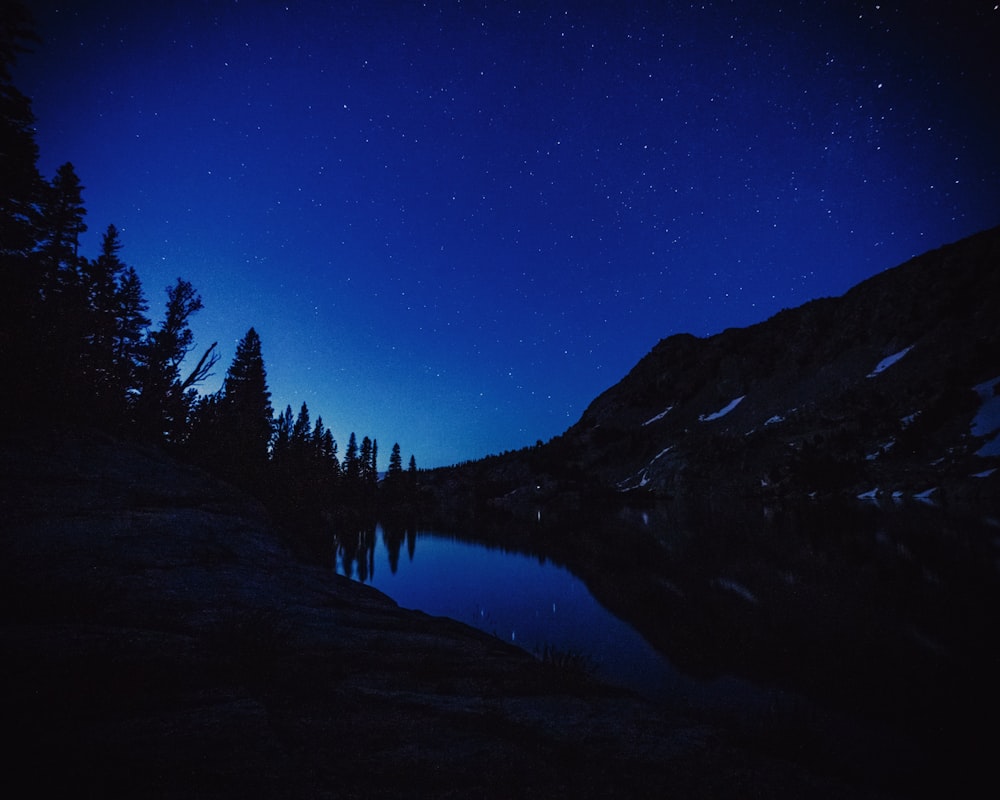 body of water beside mountain and trees