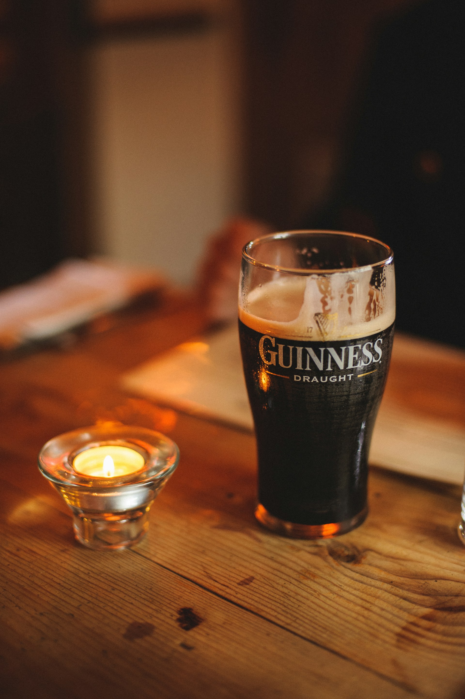 Close-up of a frothy pint of Guinness resting on a rustic wooden table, surrounded by subtle green shamrocks and dim, inviting lighting.