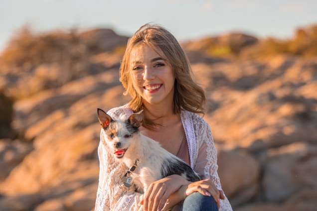 A joyful woman and her dog wearing coordinated vintage-inspired scarves and bows, smiling in a sunlit park.