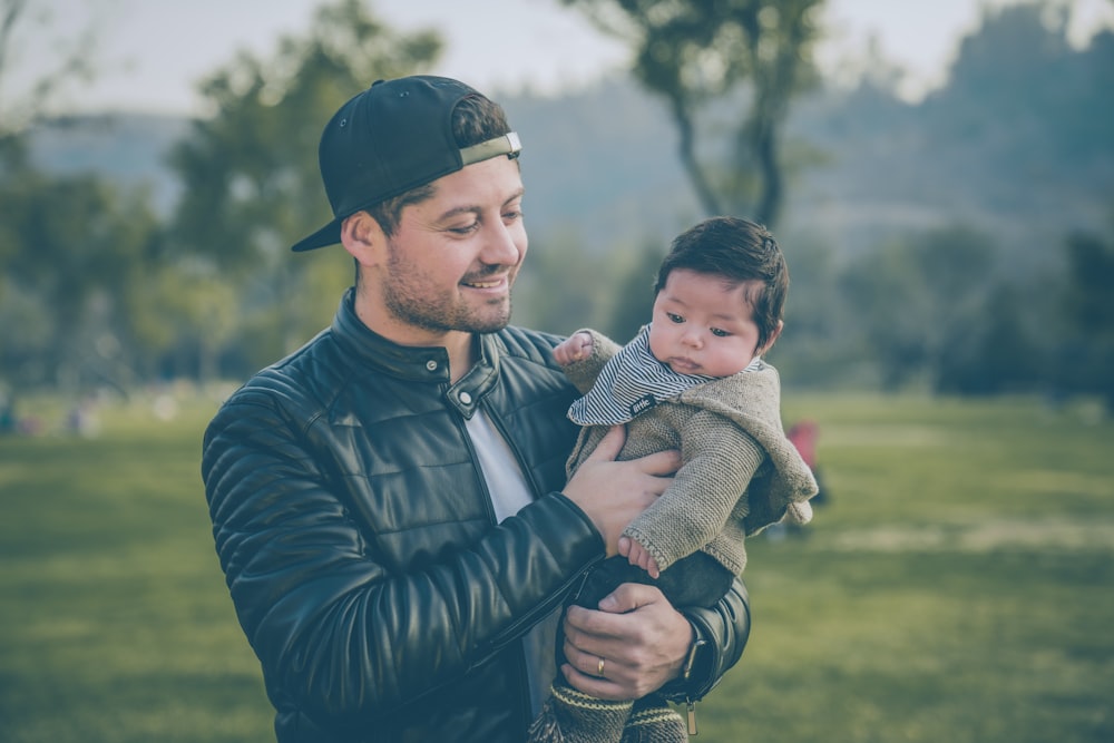 man wearing black leather jacket holding baby