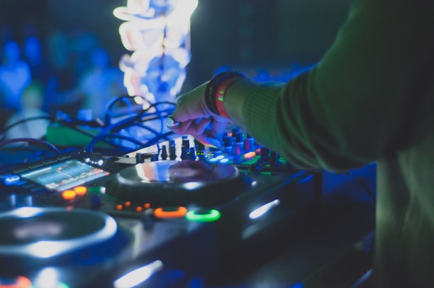 Close-up of DJ hands mixing music on turntables with neon lights reflecting.