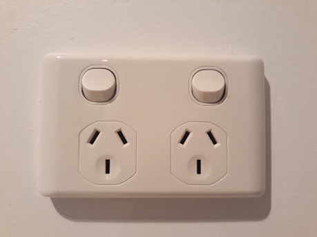 An electrical wall socket with two outlets and individual power switches, set against a light-colored wall.