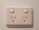 An electrical wall socket with two outlets and individual power switches, set against a light-colored wall.