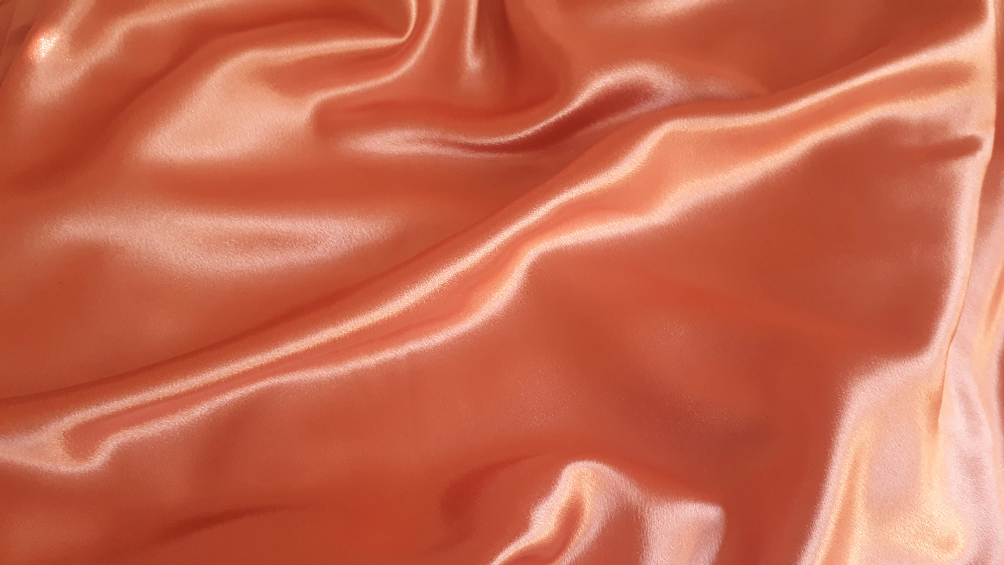 Folds of warm orange satin fabric catching soft light