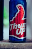 A beverage can with a red and blue design, featuring prominent branding in white text. The can has condensation on its surface, indicating it is cold. The background is slightly blurred, bringing focus to the can.