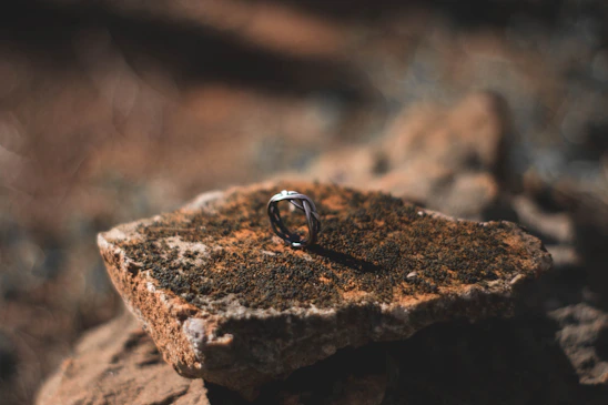 Close-up of a handmade silver ring resting on a smooth stone, highlighting its organic, imperfect shape.