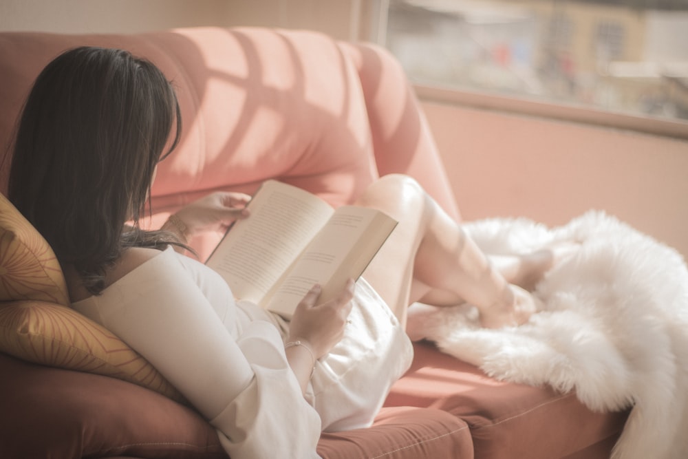 ピンクの布製ソファに座って本を持っている女性