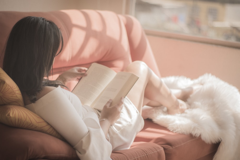 woman holding book sitting on pink fabric sofa