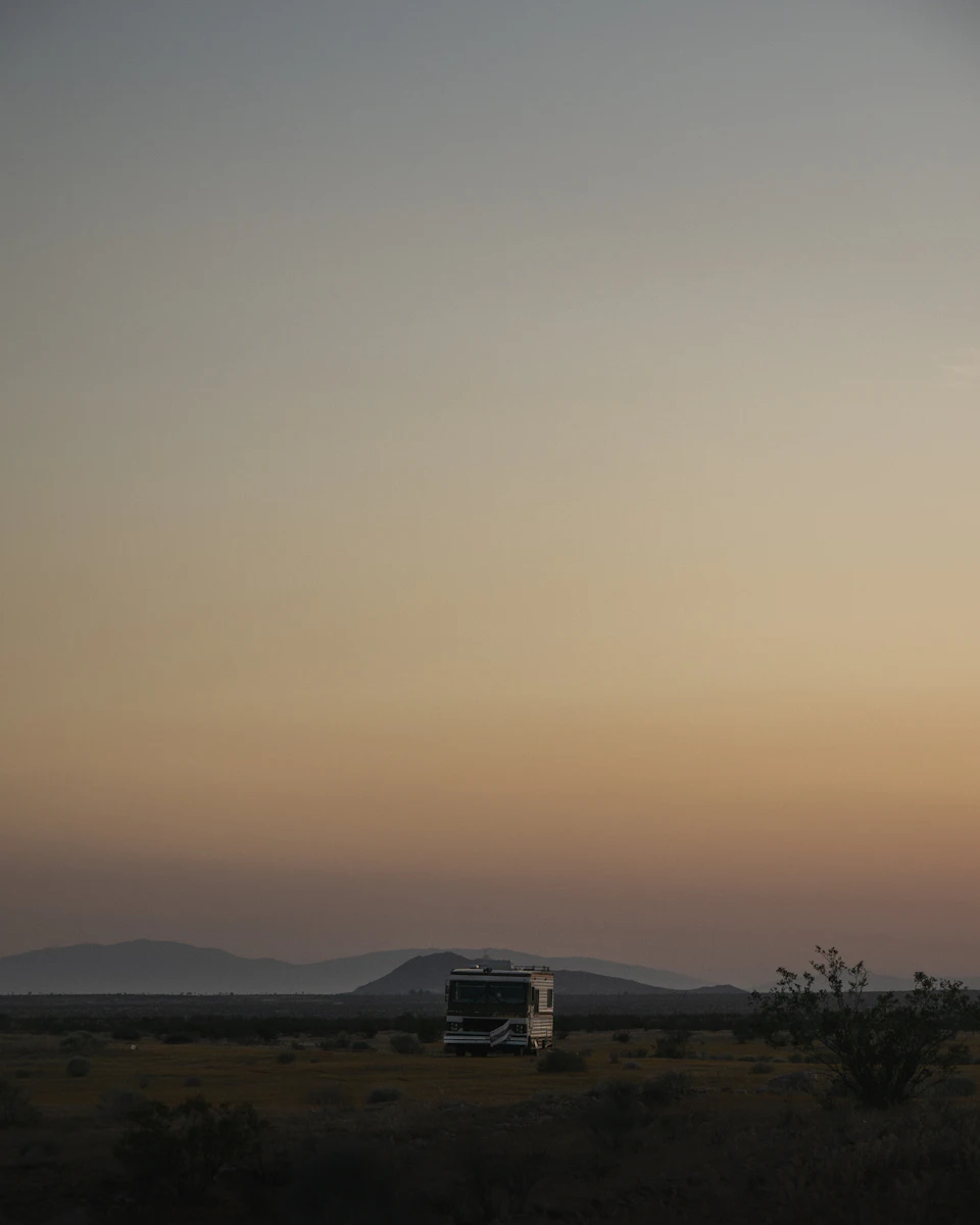 White camper van parked on desert dirt road at sunset with orange-pink sky