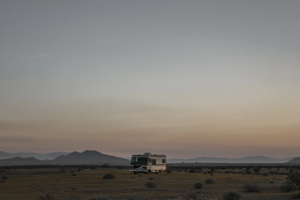 Serene desert landscape at sunset features a white and black camper van on a dirt