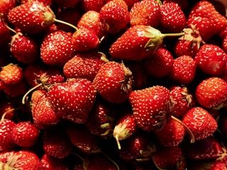 A pile of fresh, ripe strawberries with vibrant red color and small seeds visible on the surface, displaying a natural, organic texture.