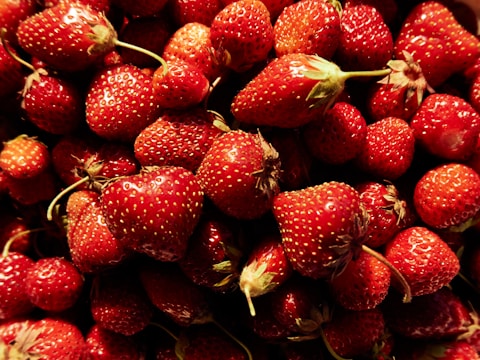 A pile of fresh, ripe strawberries with vibrant red color and small seeds visible on the surface, displaying a natural, organic texture.