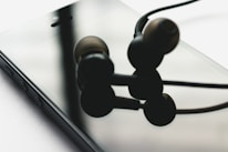 Close-up of hands holding a smartphone with stylish headphones and charger accessories nearby.