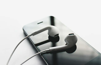 Minimalist Apple-style earbuds placed beside a smartphone with a dark theme wallpaper