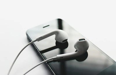 Minimalist Apple-style earbuds placed beside a smartphone with a dark theme wallpaper