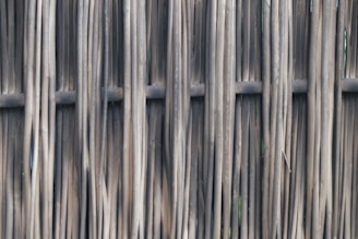 A tightly woven wooden fence made of vertical sticks or poles, creating a textured and natural appearance.