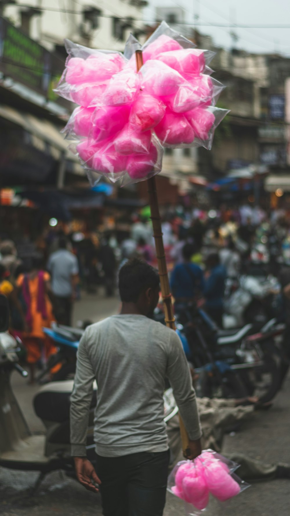 Person mit grauem langärmeligem Hemd trägt Stock mit rosa Zuckerwatte