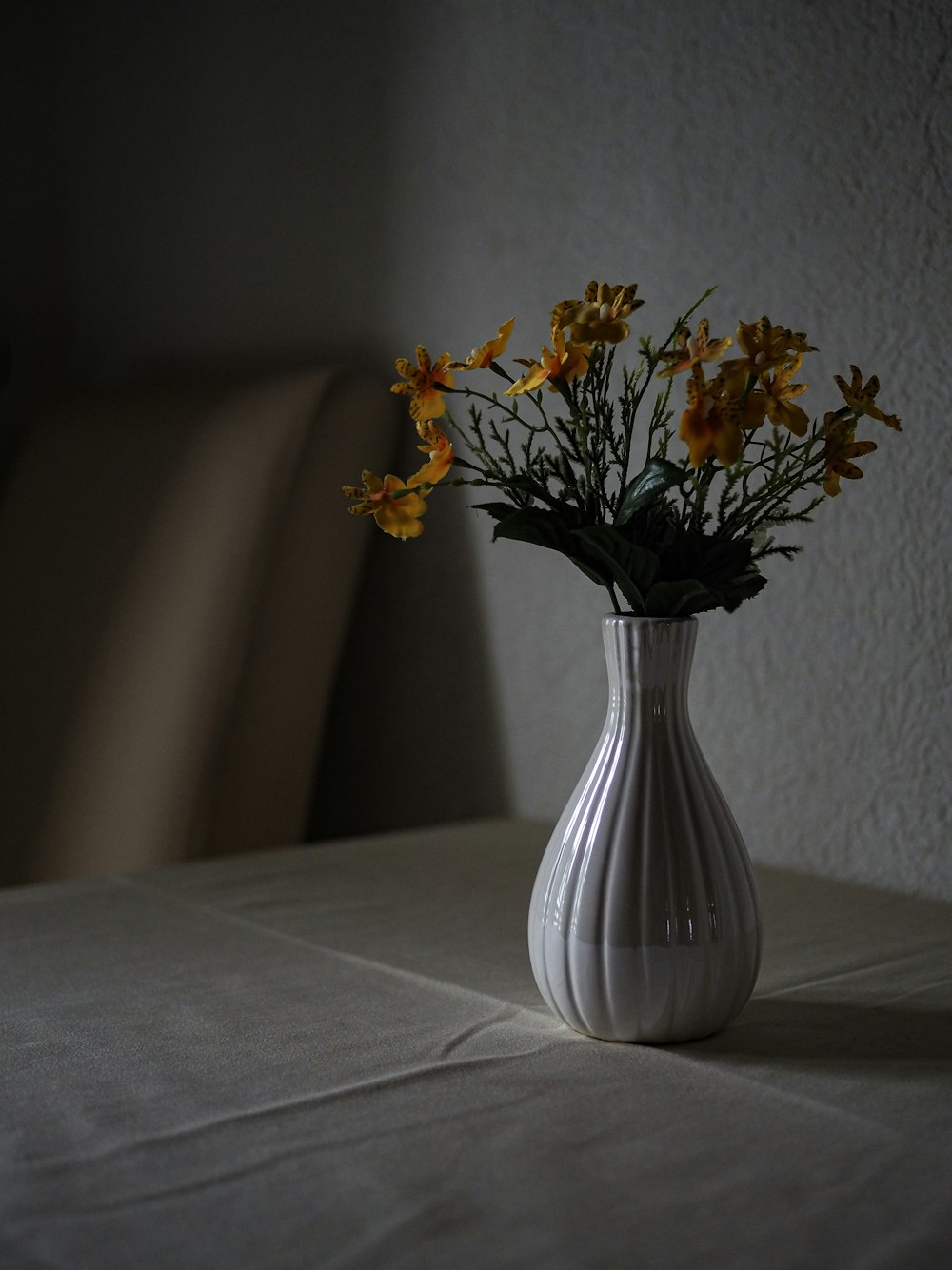 un vaso bianco pieno di fiori gialli su un tavolo