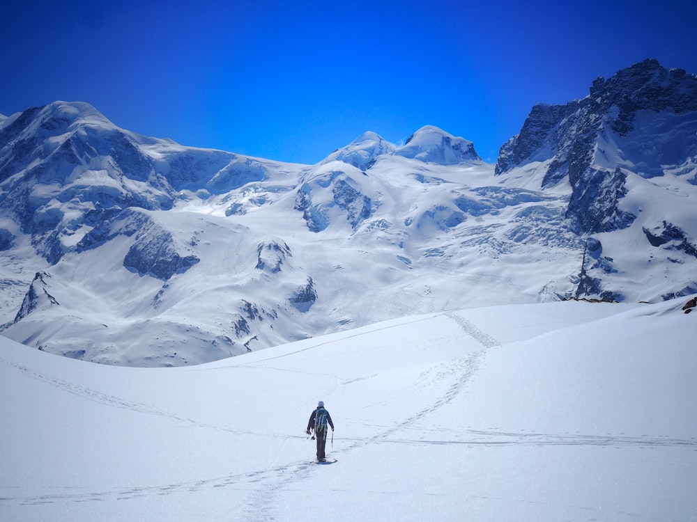 man walking on snow covered area under blue sky