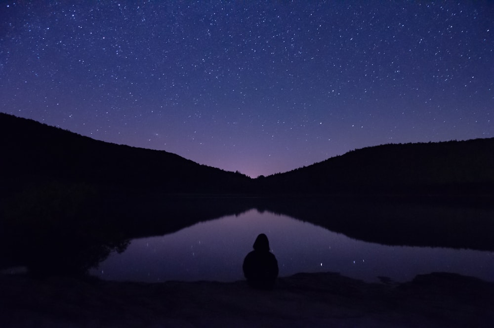 a person sitting in front of a lake under a night sky